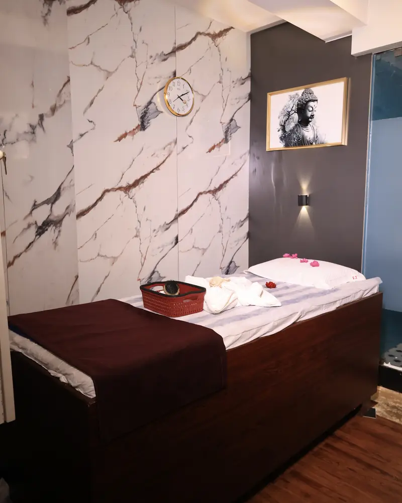 Massage room at Amron Spa with marble-effect walls, a gold-framed Buddha artwork and a freshly prepared massage bed