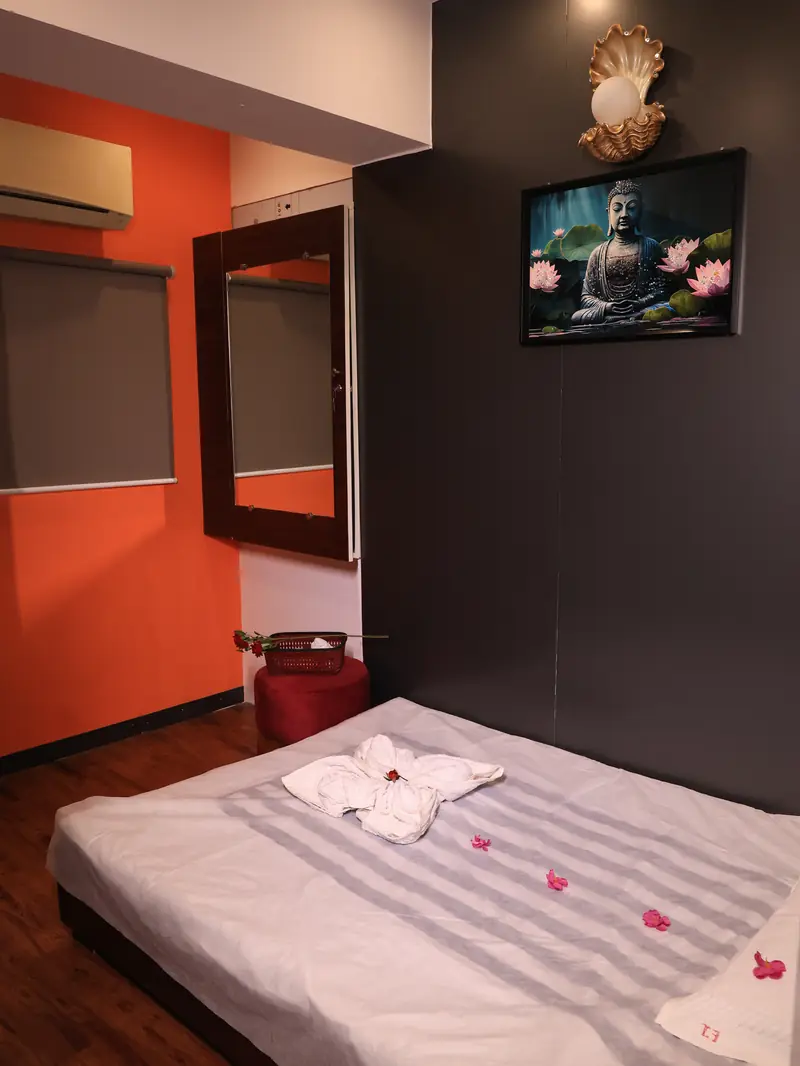 Therapy room with an orange feature wall, mirror and a massage bed set with a folded towel and flower petals
