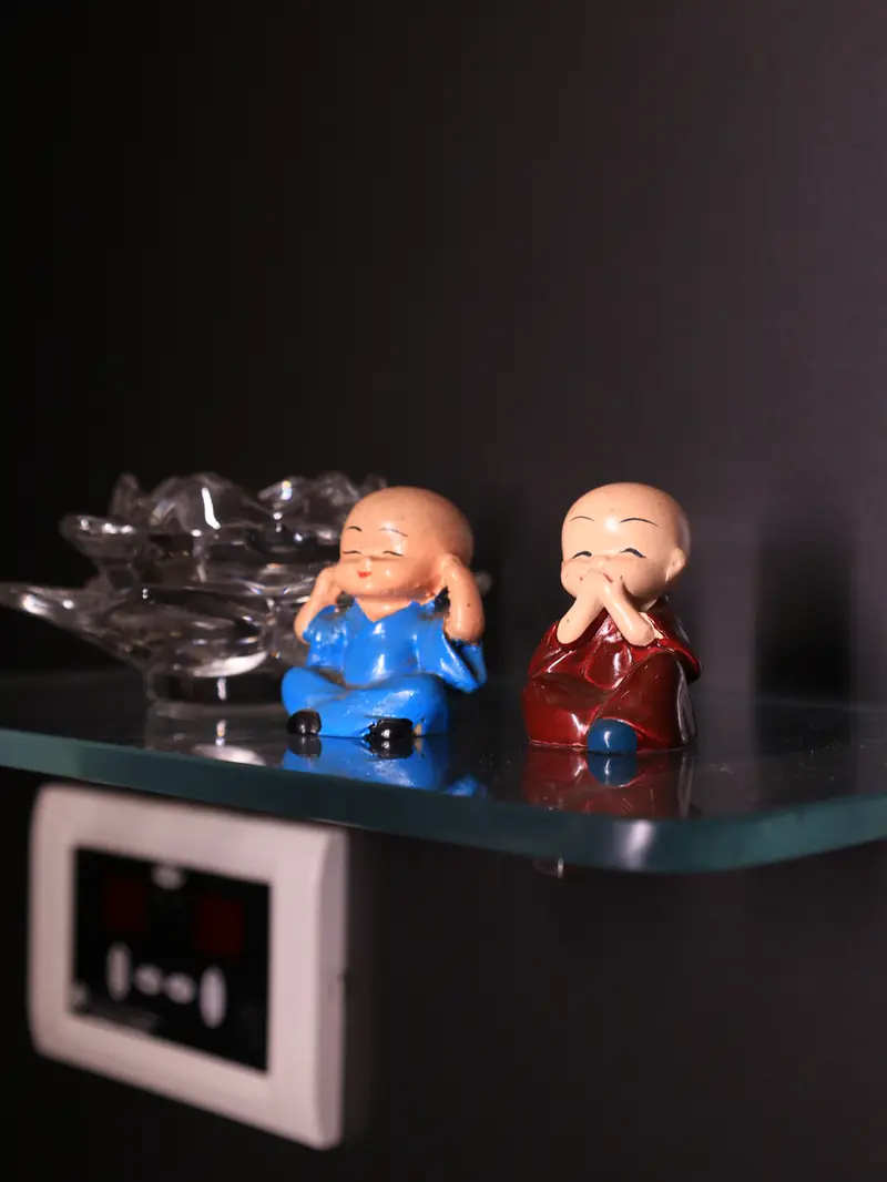 Small monk figurines and a glass lotus bowl on a shelf